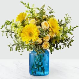 Yellow gerbera daisies and roses in a blue glass vase