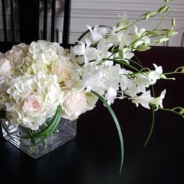 White and pale pink floral arrangement in a square glass vase