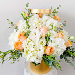 White and peach floral arrangement in a gold hatbox-style container