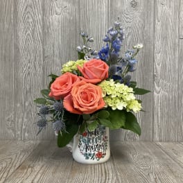 Coral roses and blue flowers in a printed mug vase