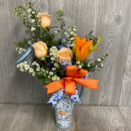 Mixed bouquet with peach roses, orange lilies, and small white daisies in a patterned tumbler