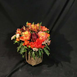 Orange and red mixed flower arrangement in a textured vase