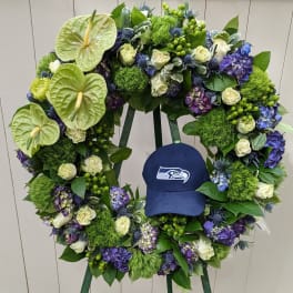 Large floral wreath with white roses, purple hydrangeas, and green anthuriums around a blue cap