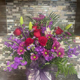 Purple and red mixed flower arrangement in a white vase with a ribbon