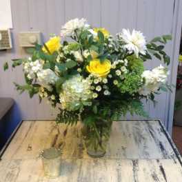 Yellow roses and white flowers arranged in a clear glass vase