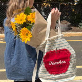 Person carrying a bouquet of yellow flowers and a striped tote bag
