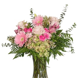 Pink roses, gerbera daisies, carnations, and green hydrangea in a clear glass vase