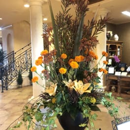 Tall floral arrangement with orange blooms in a black urn vase