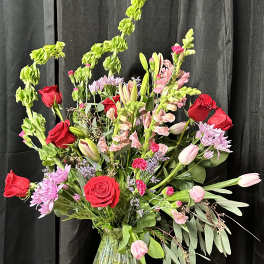 Mixed bouquet of red roses, pink tulips, and lilies in a glass vase