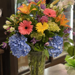 Colorful mixed bouquet in a clear glass vase with blue hydrangeas and gerbera daisies
