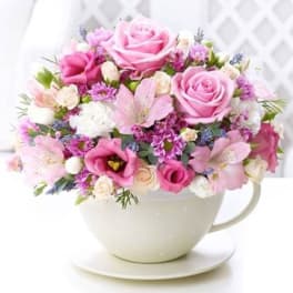 Pink and white flower arrangement in a teacup vase on a saucer