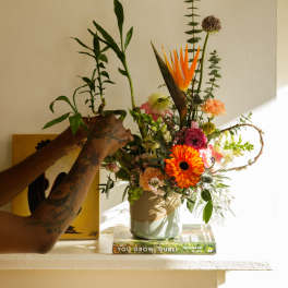 Colorful mixed flower arrangement with bird of paradise and orange gerbera daisies in a ceramic vase.