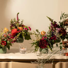 Three floral arrangements in green vases on a table with candles and scissors