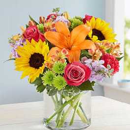 Bouquet of sunflowers, orange lilies, and pink roses in a glass vase