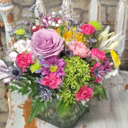 Colorful mixed flower arrangement with lavender rose, pink carnations, and daisies in a square glass vase