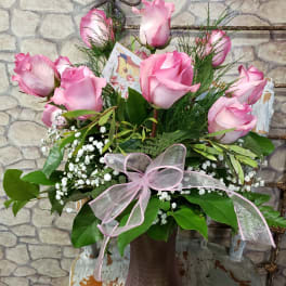 Arrangement of pink roses and white baby’s breath in a mauve glass vase with a pink ribbon bow.