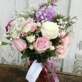 Pink and white rose bouquet in a glass vase with purple flowers