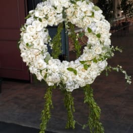 Large white floral wreath on an easel with trailing greenery