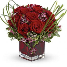 Red roses arranged in a square glass vase with looping grass accents