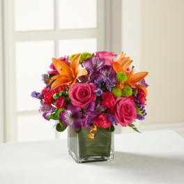Colorful bouquet of roses, lilies, and purple flowers in a glass vase