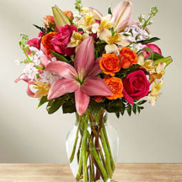 Mixed bouquet of pink lilies, roses, and orange blooms in a glass vase