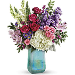 Mixed bouquet of roses, hydrangeas, and purple flowers in a blue glass vase