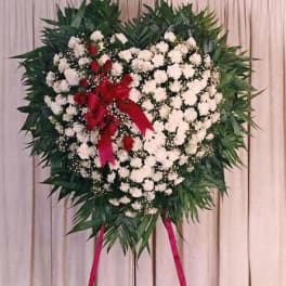 Heart-shaped floral wreath with white flowers and red roses on a stand