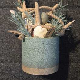 Coastal arrangement of driftwood, rope, and seashells in a blue ceramic pot with faux foliage.