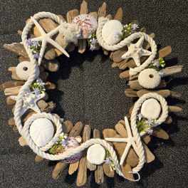 Driftwood wreath decorated with white rope, seashells, and small purple-white flowers