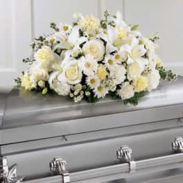 White floral casket spray with roses, lilies, and daisies