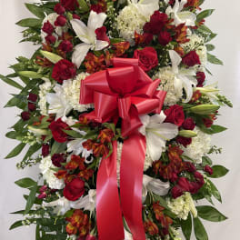Standing floral spray with red roses, white lilies, and a red ribbon bow