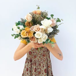 Person holding a bouquet of peach, white, and yellow roses