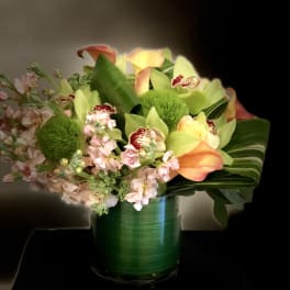 Bouquet of calla lilies, orchids, and pink flowers in a green glass vase