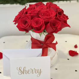Red roses in a white vase with a red ribbon and a name card