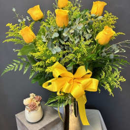 Yellow roses arranged in a tall vase with a large yellow ribbon
