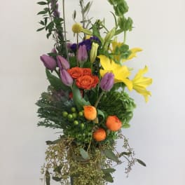 Tall mixed bouquet with yellow lilies, purple tulips, and orange roses in a glass vase