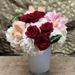 Red roses and white hydrangeas in a white vase with pink orchids
