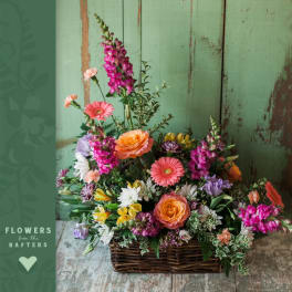 Mixed flower arrangement in a wicker basket with pink, orange, yellow, and white blooms