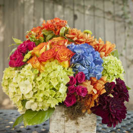 Colorful bouquet of hydrangeas, roses, and dahlias in a rustic container