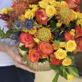 Bouquet of yellow and coral roses with blue thistle in a gold wrap