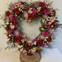 Heart-shaped floral wreath with red roses and pink blooms on a wood base