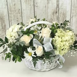 White roses and hydrangeas in a white basket with a ribbon