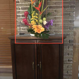 Tropical flower arrangement with orange heliconia and orchids in a white vase
