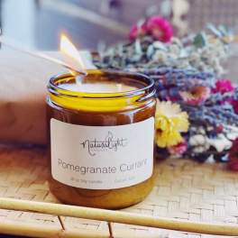 Amber glass jar pomegranate currant candle being lit on a woven tray with dried flowers behind