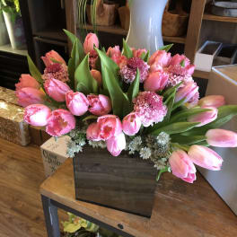 Pink tulips and carnations arranged in a dark square box