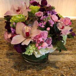 Low arrangement of pink orchids, roses, carnations, and hydrangeas in a clear glass vase
