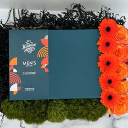 Men's soap gift box with bright orange gerbera daisies and roses, green moss and black filler in a tray