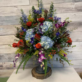 Large mixed floral arrangement in a pedestal vase with blue hydrangeas and red roses