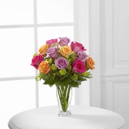 Bouquet of pink, lavender, and peach roses in a clear glass vase