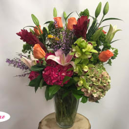 Mixed bouquet of lilies, roses, orchids, and hydrangea in a glass vase